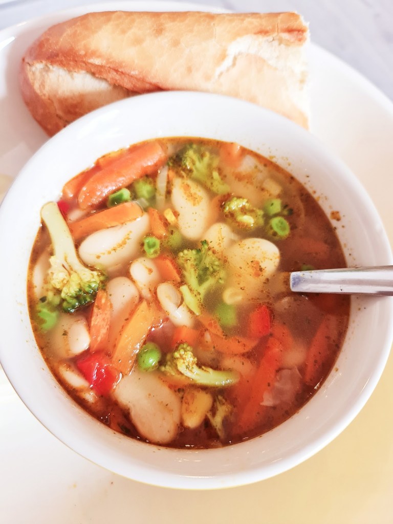A bowl of vegetable soup with beans and colorful vegetables, accompanied by a piece of bread.