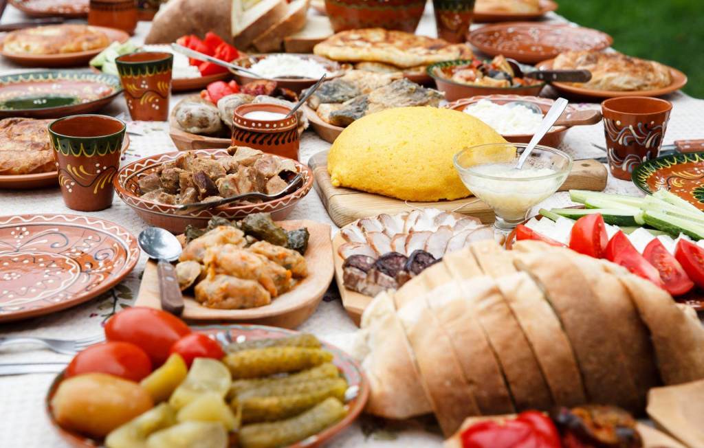 A beautifully arranged spread of traditional Romanian dishes featuring an assortment of meats, breads, and vegetables, presented on decorative plates and wooden serving boards.